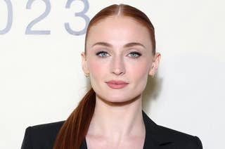 Sophie Turner poses in a deep V-neck black blazer with a sleek, long ponytail