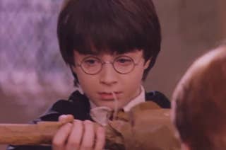 Harry Potter wearing round glasses, holds a wooden broomstick, looking intently at it